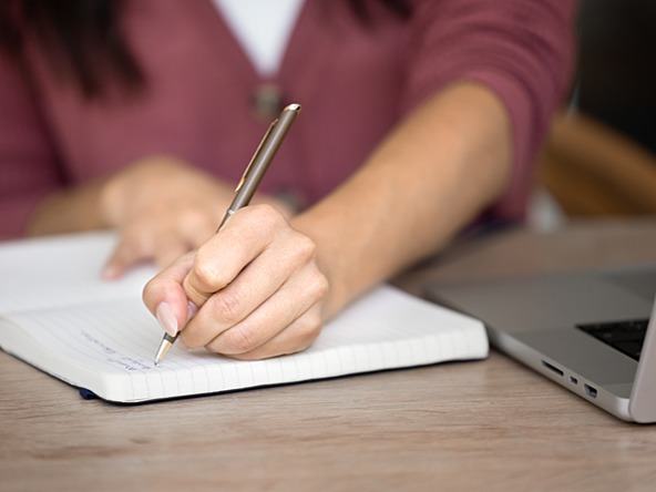 researcher taking notes in notebook next to laptop